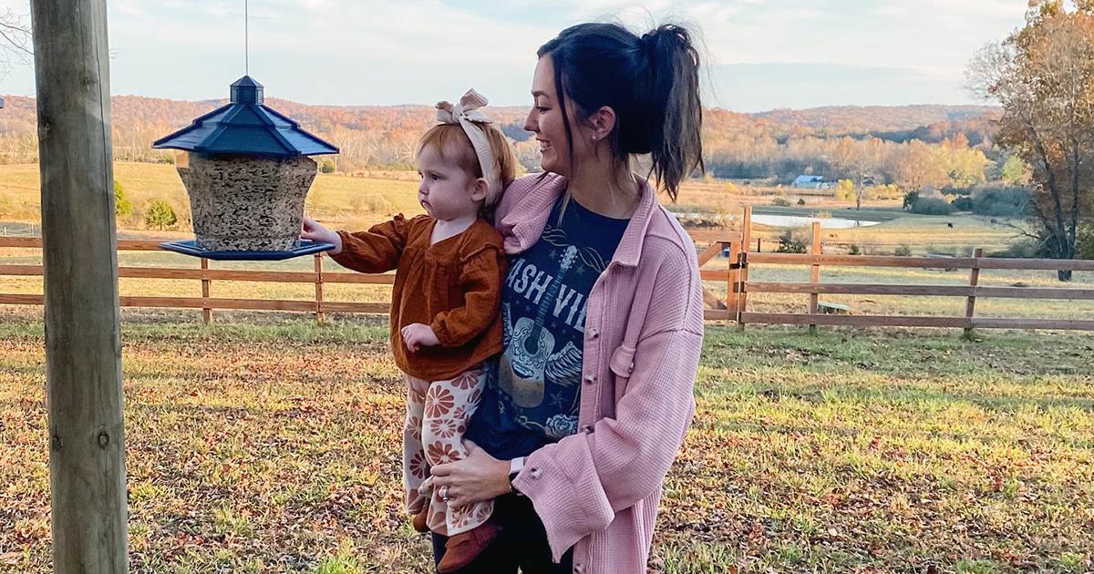 Mom and toddler looking at a hopper feeder full of seed.