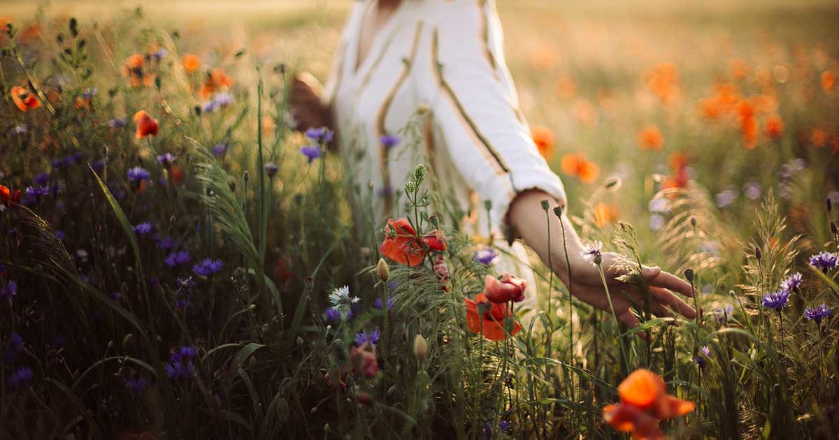 Woman walking through a meadow of wildflowers at dusk.